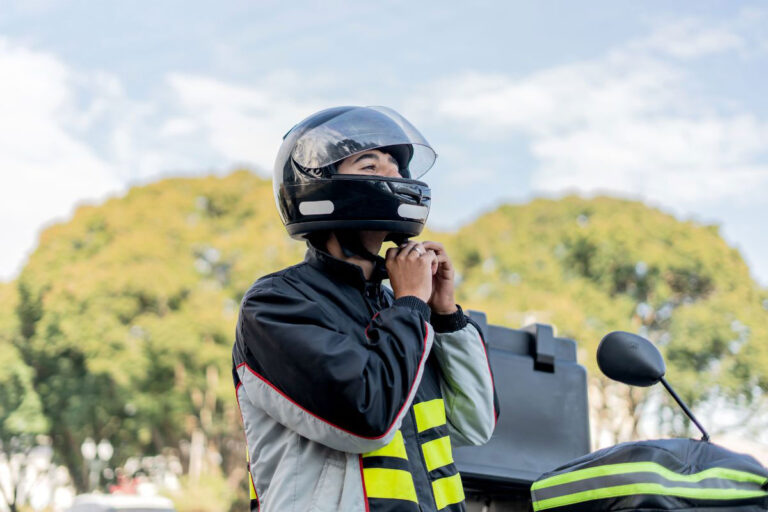 Motorcyclist securing helmet strap, wearing a safety jacket, preparing for a ride in a sunny outdoor setting.